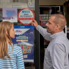 Un commerçant partenaire montre à un mineur une affiche d'information sur l'interdiction du jeu au moins de 18 ans